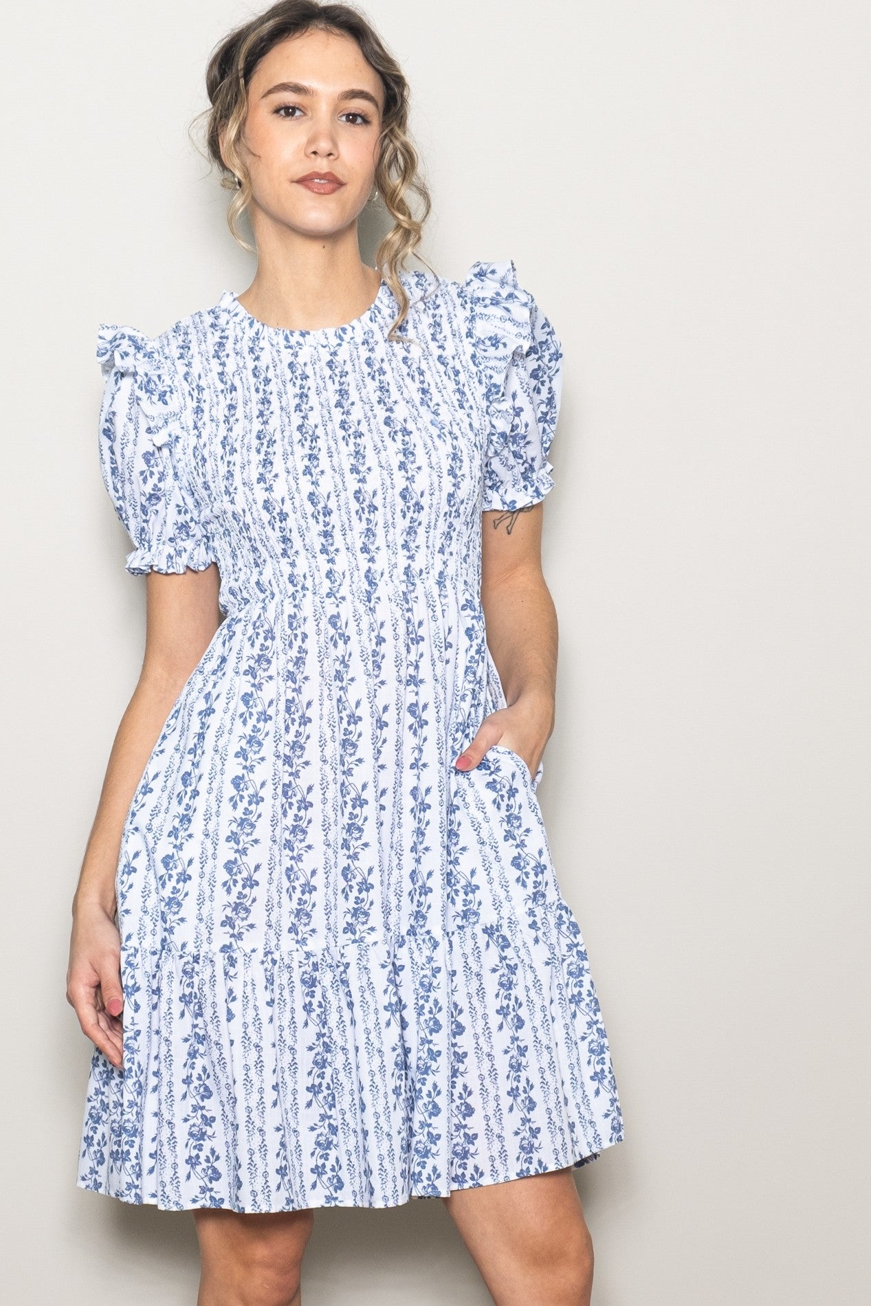 woman wearing a white short sleeve dress with blue floral pattern and puff sleeves, standing with one hand on her hip