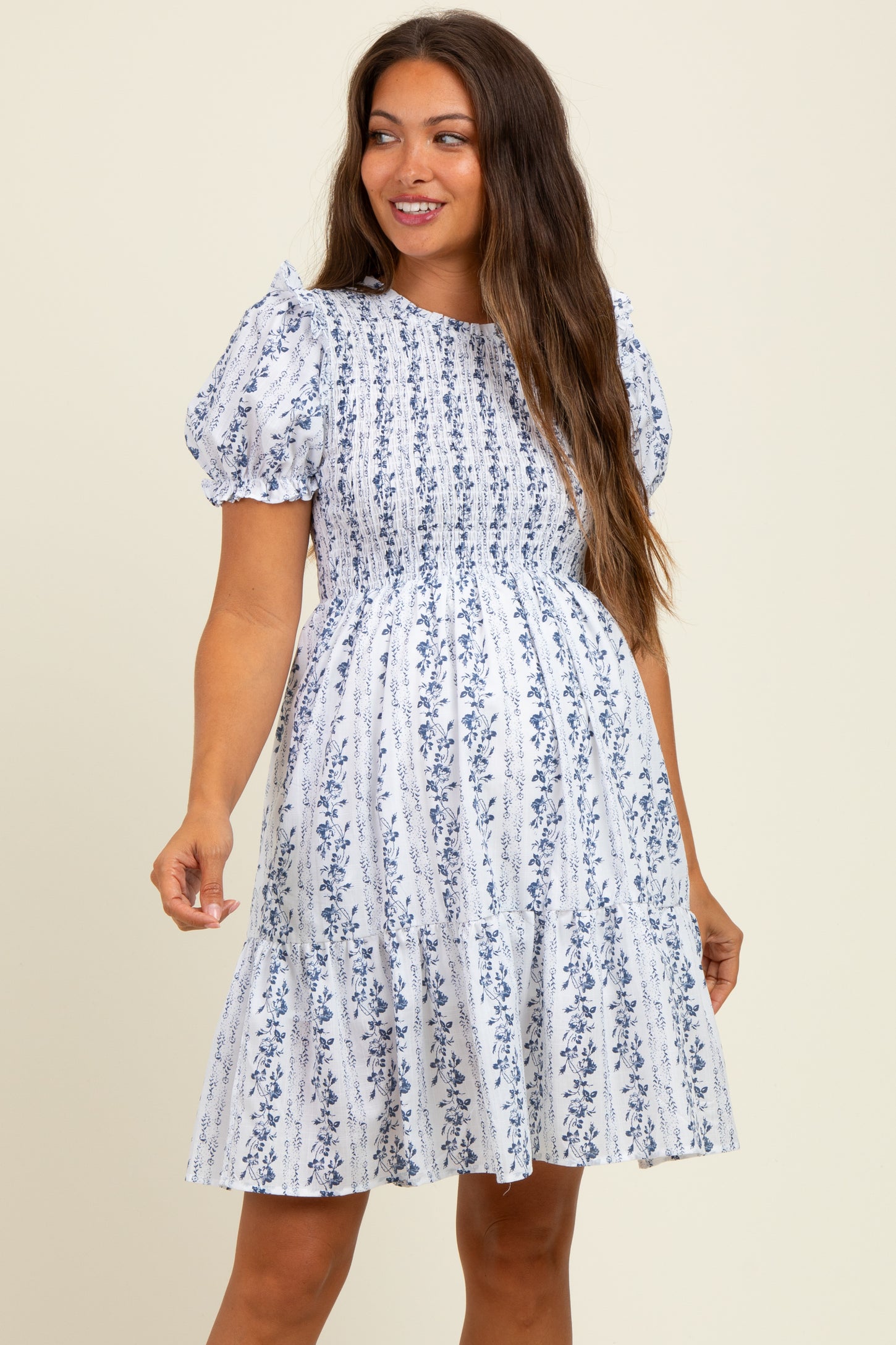 woman wearing a white floral maternity dress with short puff sleeves and a smocked bodice, showcasing her baby bump