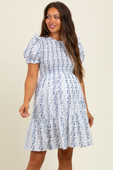 woman wearing a white floral maternity dress with short puff sleeves and a smocked bodice, showcasing her baby bump