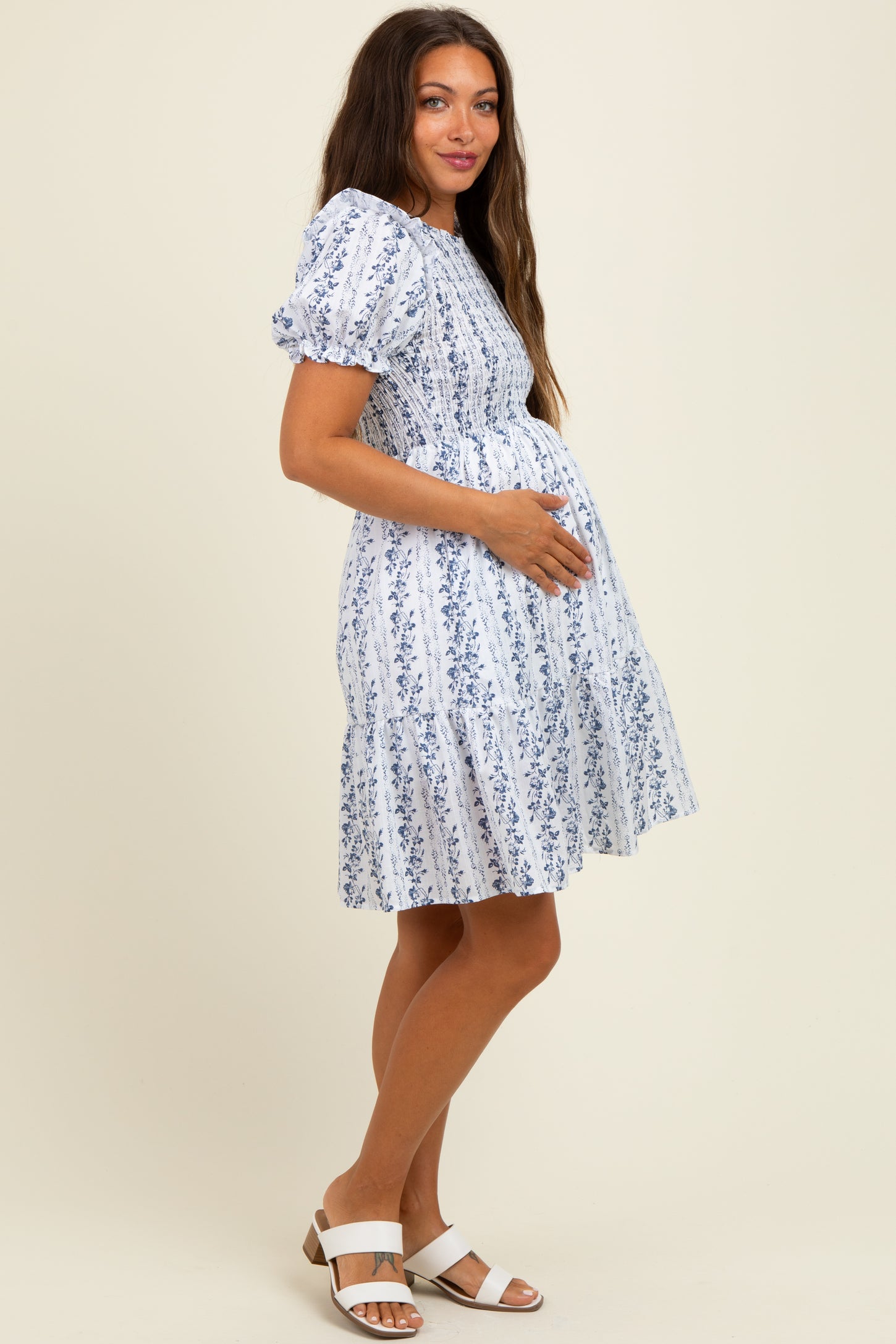 woman wearing a white floral puff sleeve maternity dress and holding her baby bump
