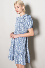 woman wearing a blue floral print short sleeve dress with ruffle details and a tiered skirt