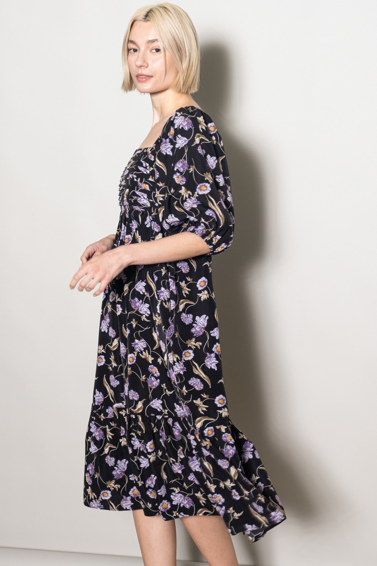 woman wearing a black floral mid-length dress with puff sleeves and a tiered skirt.