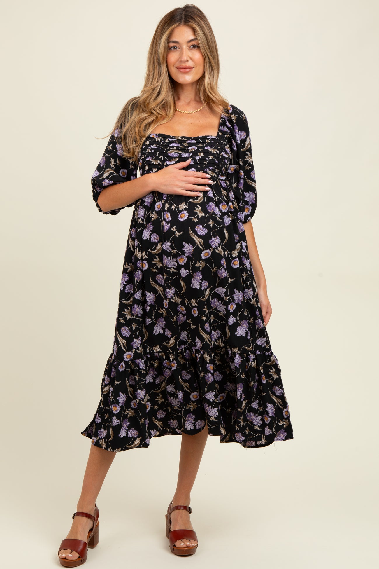 woman wearing a black floral maternity dress with a ruffled hem and gathered bust, holding her baby bump