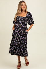 woman wearing a black floral maternity dress with puff sleeves and a tiered skirt, showcasing her baby bump