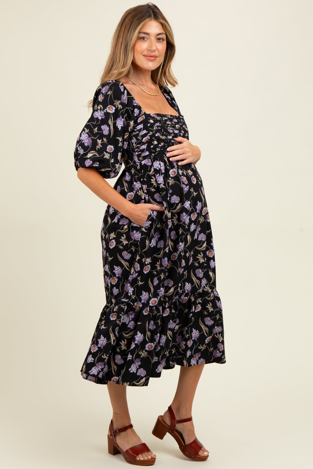 woman wearing a black floral maternity dress with puff sleeves and a ruffled hem, holding her baby bump