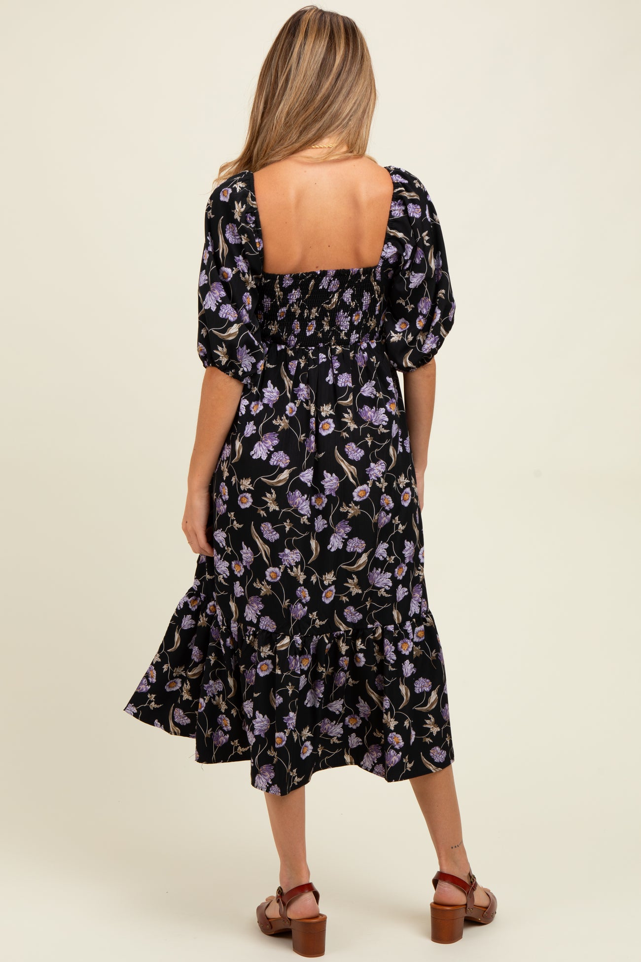 woman wearing a black floral maternity dress with short puff sleeves and a flowy skirt, showing a baby bump from the back