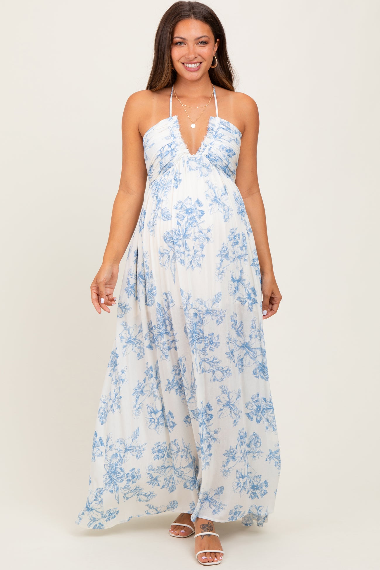 woman wearing a floral print maxi maternity dress in white and blue with a deep neckline and halter straps