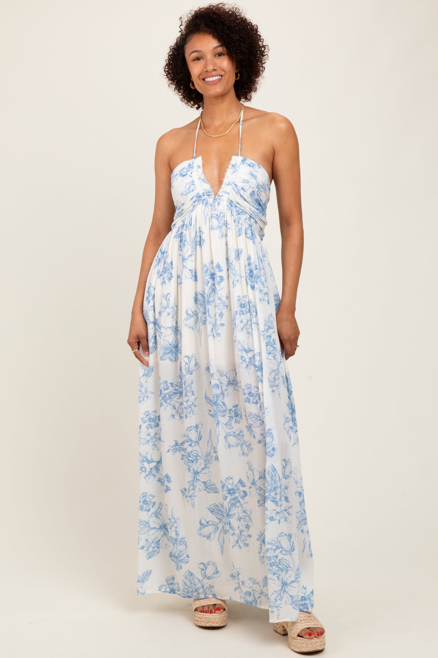 woman wearing a white floral maxi dress with blue print and halter neckline, smiling at the camera