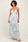 woman wearing a white floral maxi dress with blue print and halter neckline, smiling at the camera