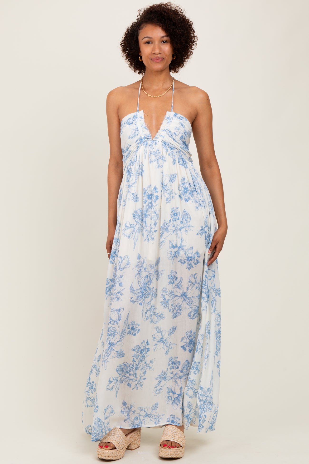 woman wearing a white maxi dress with blue floral print and a halter neckline, standing confidently