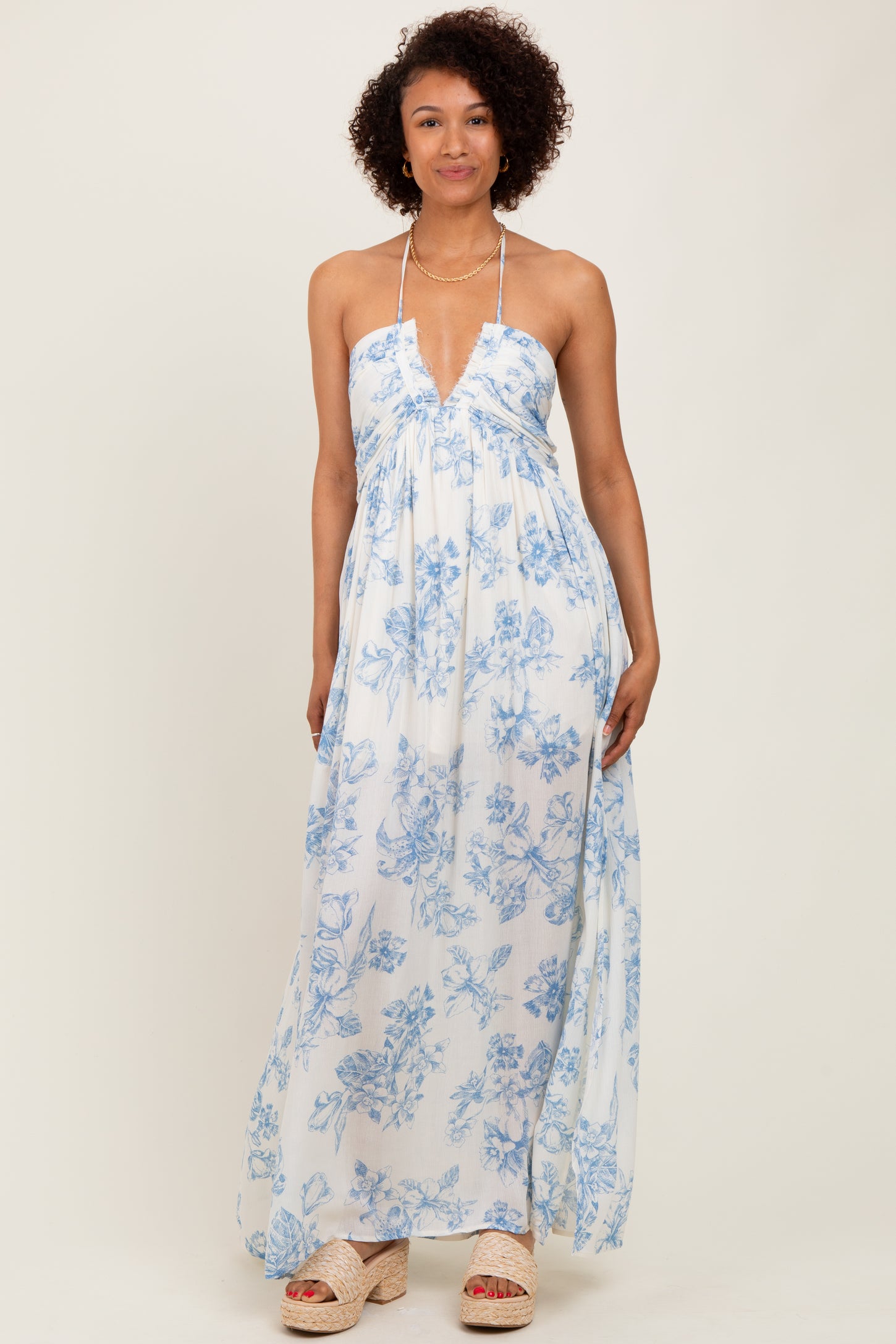woman wearing a white maxi dress with blue floral print and a halter neckline, standing confidently