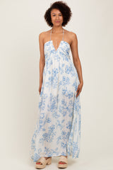 woman wearing a white maxi dress with blue floral print and a halter neckline, standing confidently