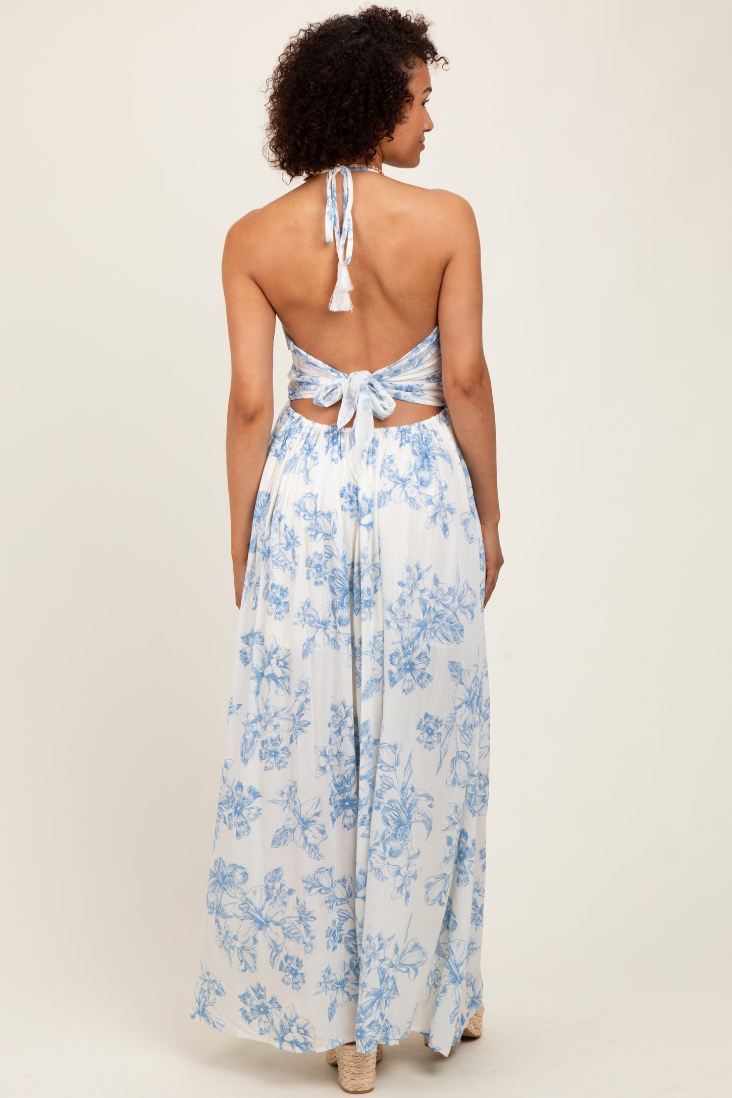 woman wearing a flowy light blue floral maxi dress with a halter neck and open back detail