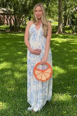 woman wearing a white floral maternity maxi dress and holding her baby bump with an orange handbag
