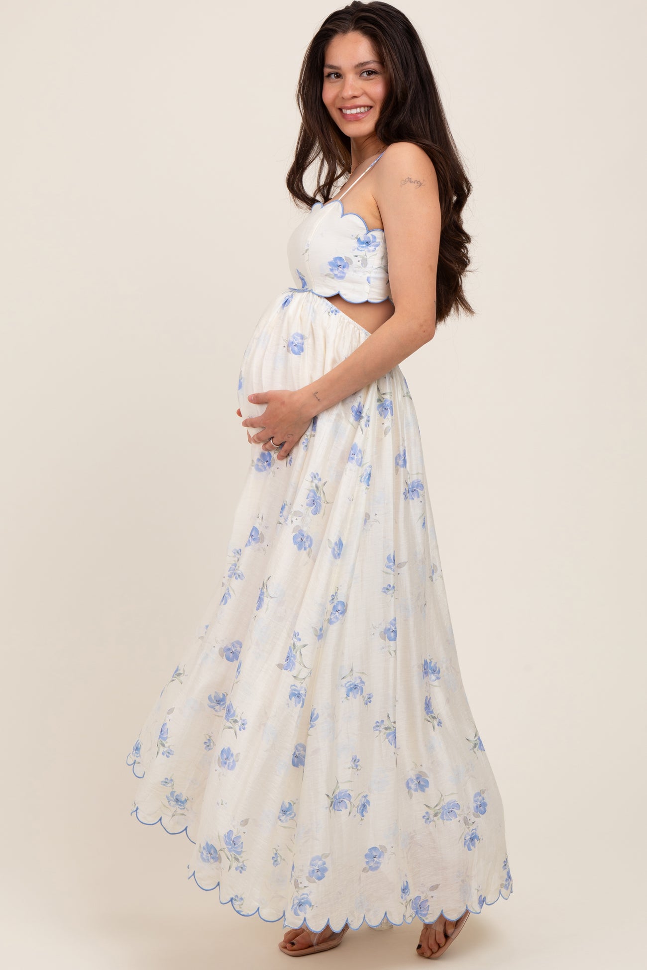 woman wearing a white floral maxi maternity dress with blue flowers, showing her baby bump and smiling