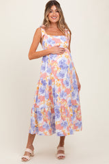 woman wearing a floral print maternity dress in pastel colors and holding her baby bump