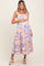 woman wearing a floral print maternity dress in pastel colors and holding her baby bump