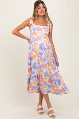 woman wearing a floral maternity maxi dress with tie straps and a flowing skirt, showing her baby bump