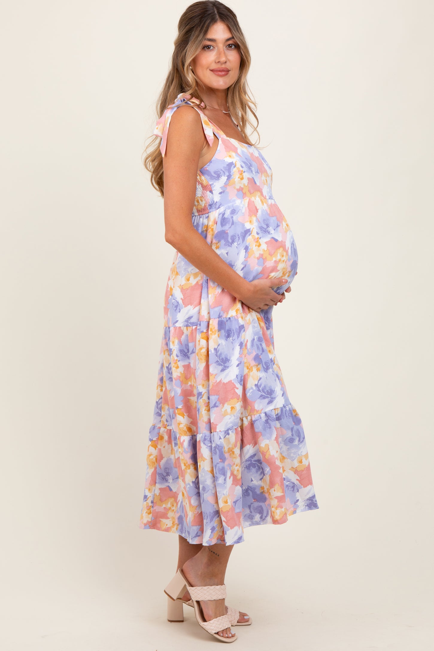 woman wearing a floral maternity dress with tied straps, cradling her baby bump