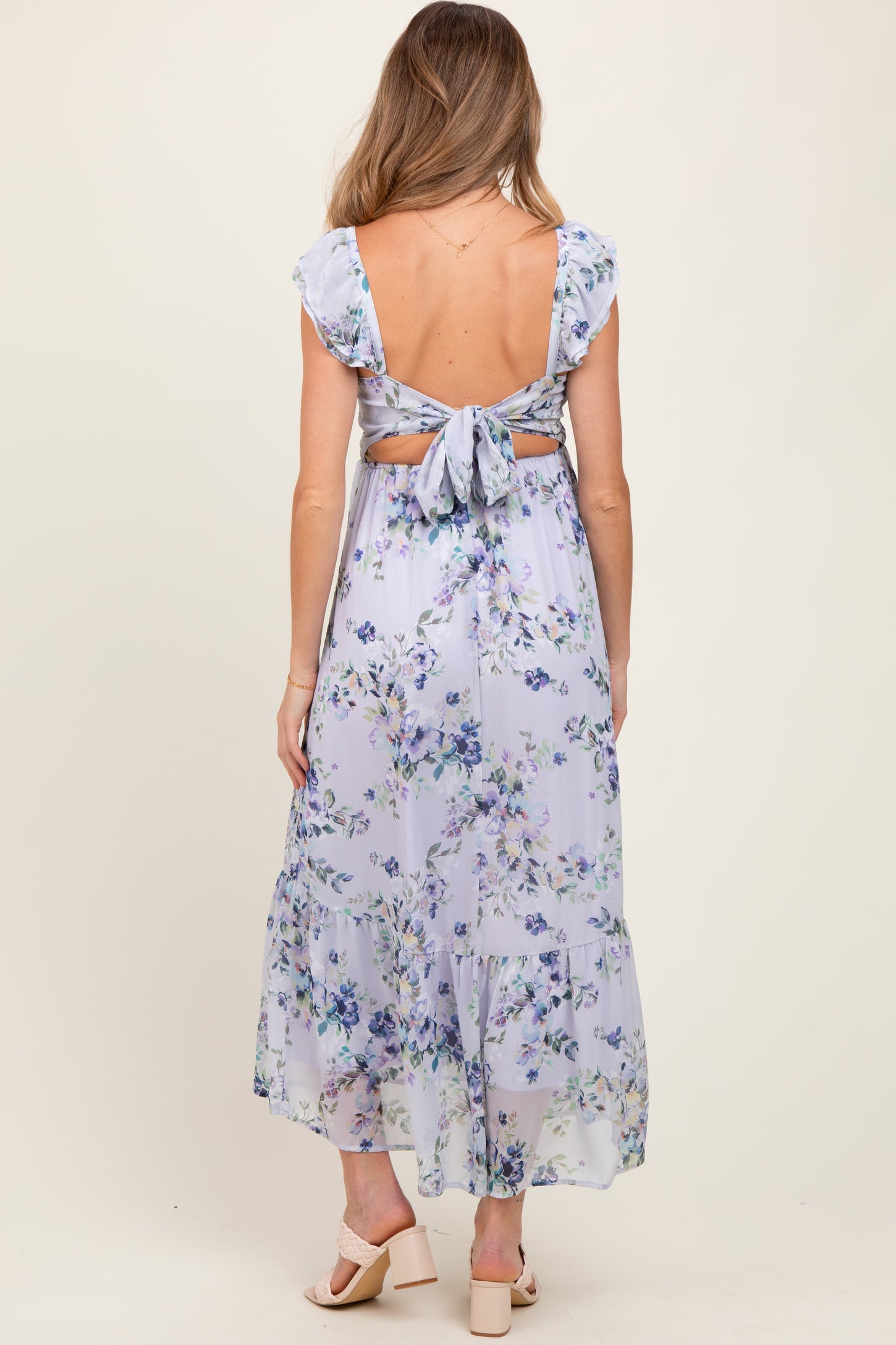 woman wearing a lavender floral maternity dress with ruffle sleeves and a tie-back detail