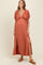 woman wearing a rust-colored maxi maternity dress with a deep V-neck and thigh-high split, showcasing her baby bump