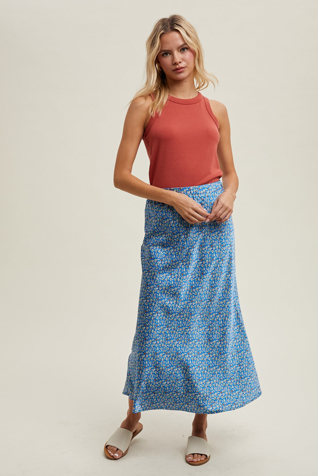 woman wearing a rust-colored sleeveless top and a blue floral maxi skirt with a relaxed fit
