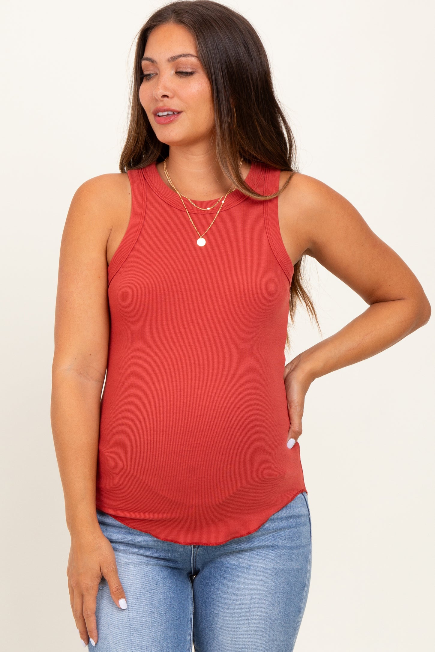 woman wearing a rust red ribbed maternity tank top and showing her baby bump while posing with one hand on her hip