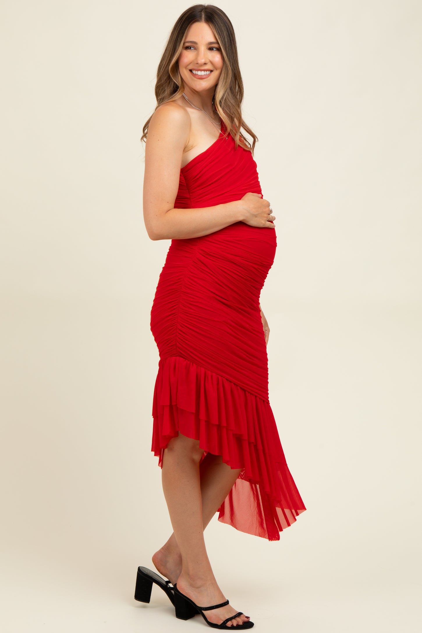 woman wearing a red one-shoulder maternity dress with ruching and a flowy hemline, showcasing her baby bump