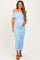 woman wearing a light blue off-shoulder maternity dress with ruched details and holding her baby bump