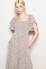 woman wearing a floral print maxi dress with a square neckline and flutter sleeves, posing with hands in pockets