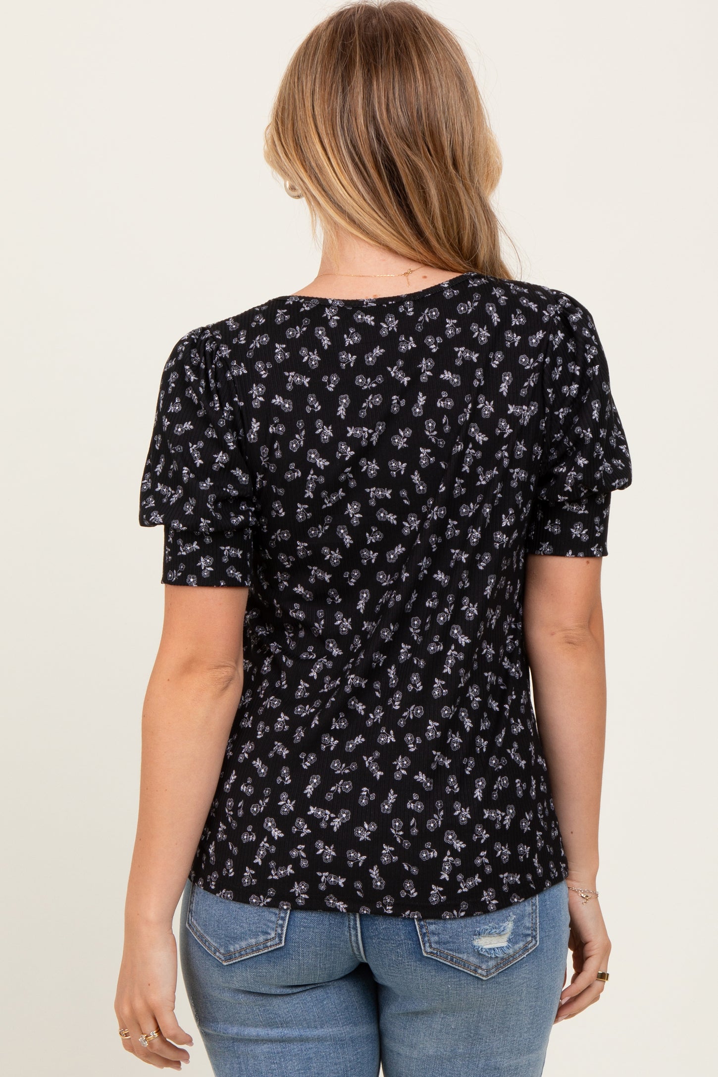 woman wearing a black floral short sleeve top with puffed sleeves, styled with blue jeans, view from the back