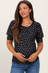 woman wearing a black short sleeve maternity top with floral print and holding her baby bump