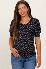 woman wearing a black floral maternity top with puff sleeves and smiling while holding her baby bump