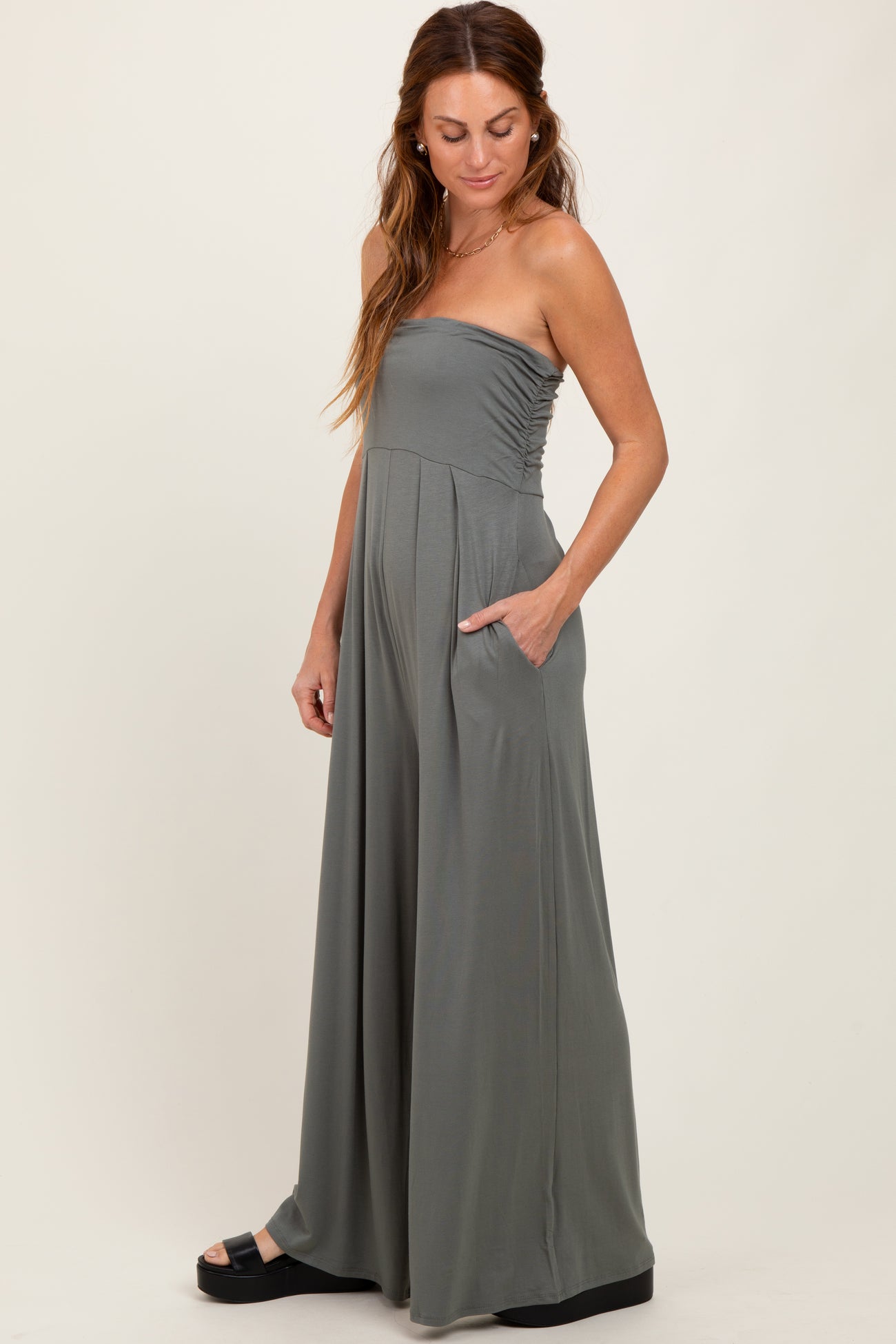 woman wearing a sage green strapless maxi dress with side pockets and a pleated design