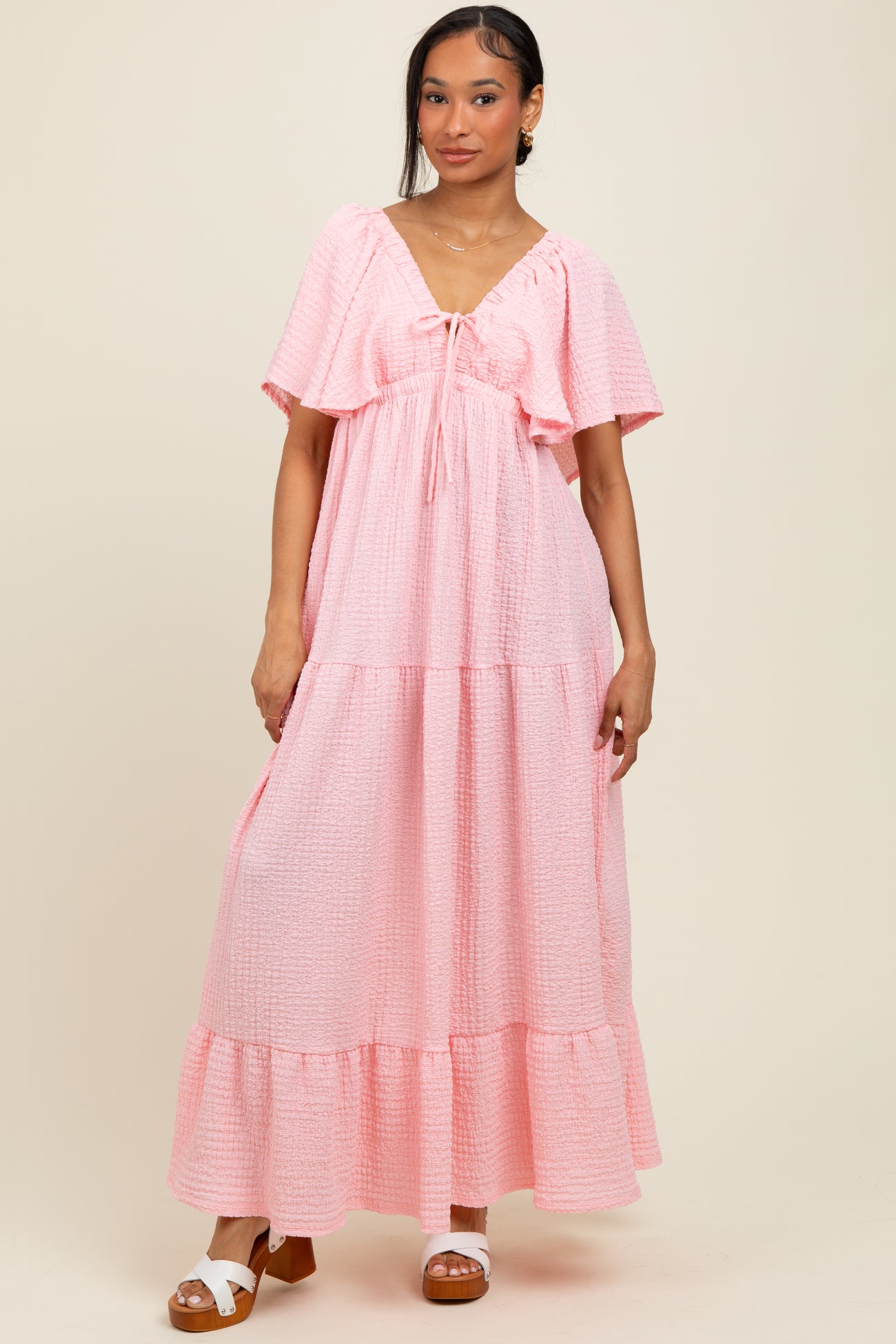 woman wearing a pink tiered maxi dress with a tie detail and flutter sleeves