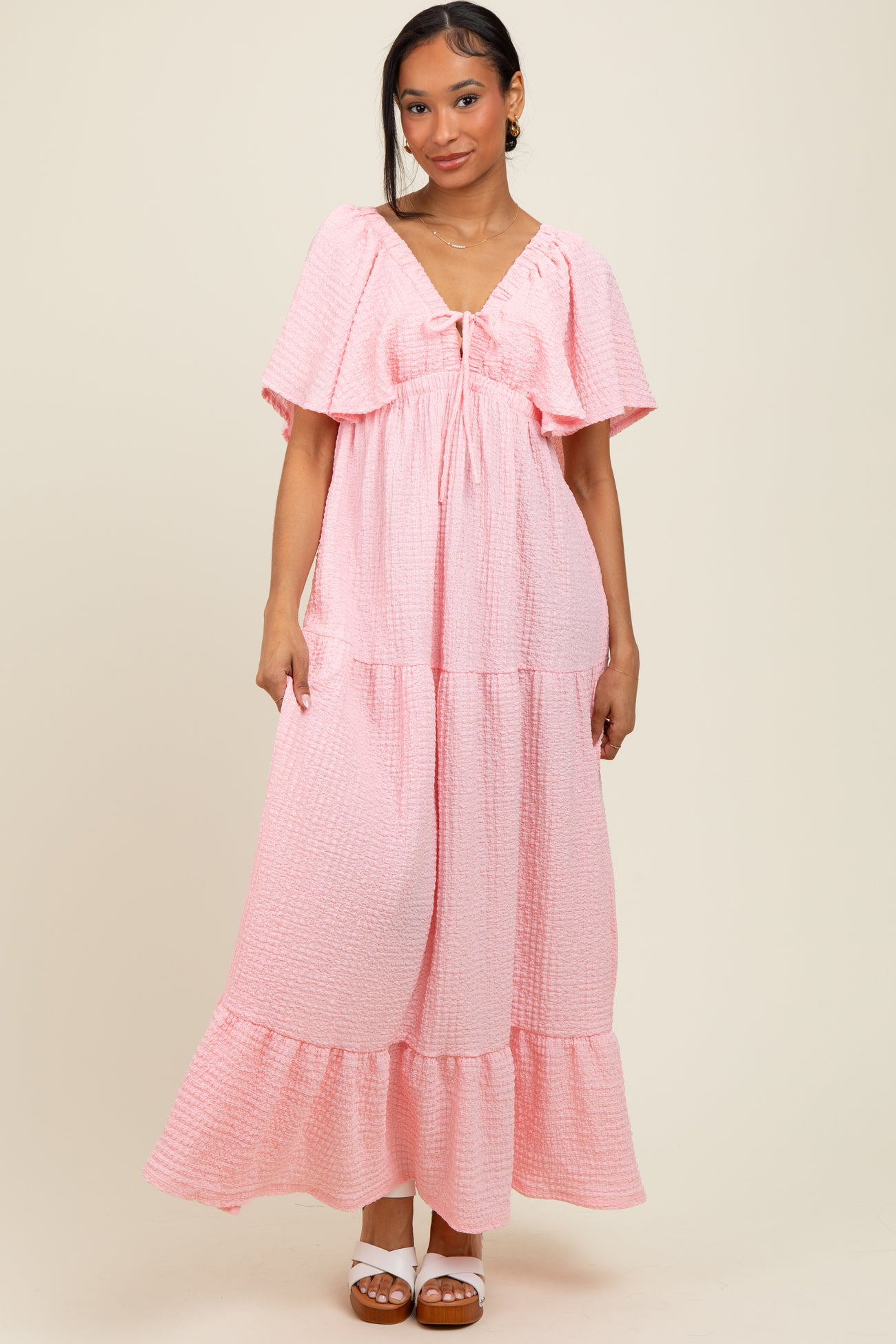 woman wearing a pink tiered maxi dress with flutter sleeves and a tie detail at the neckline