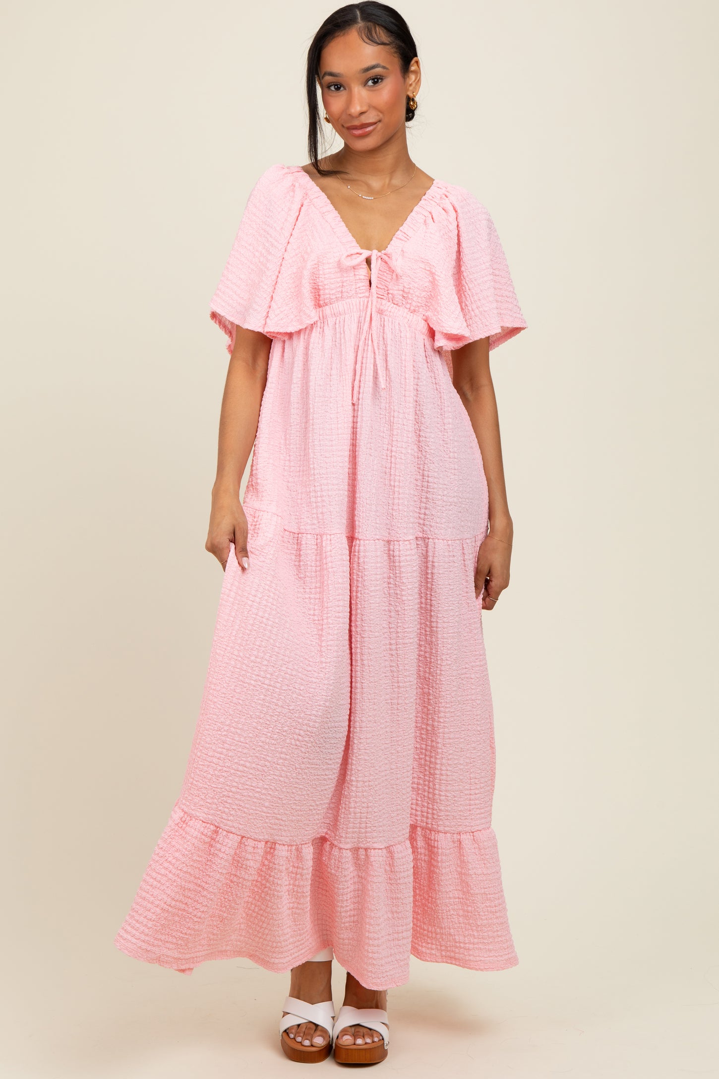 woman wearing a pink tiered maxi dress with flutter sleeves and a tie detail at the neckline