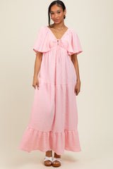 woman wearing a pink tiered maxi dress with flutter sleeves and a tie detail at the neckline