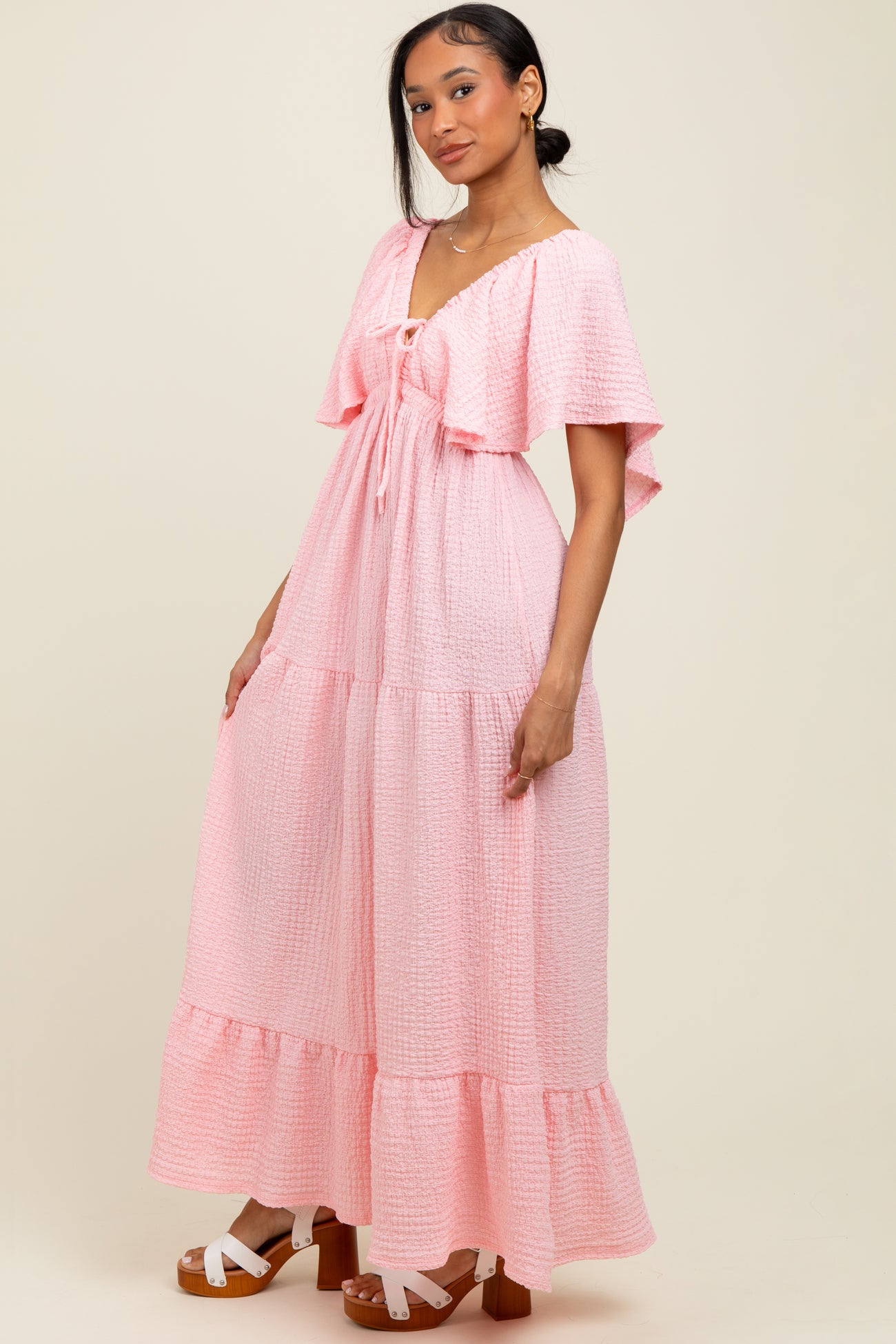 woman wearing a pink tiered maxi dress with flutter sleeves and a tie front detail