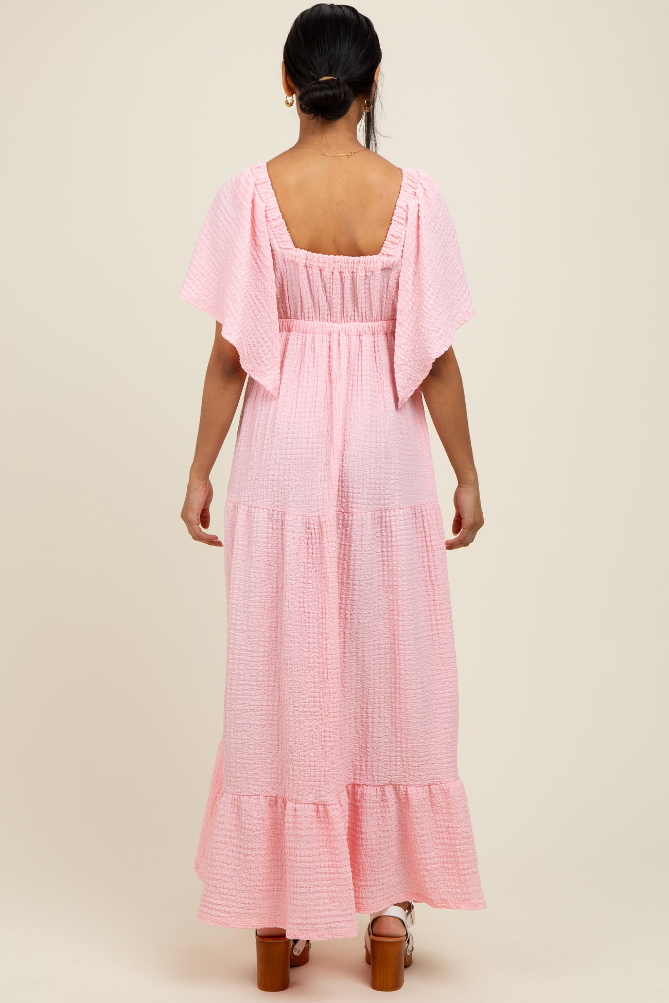 woman wearing a pink tiered maxi dress with flutter sleeves and a smocked back detail