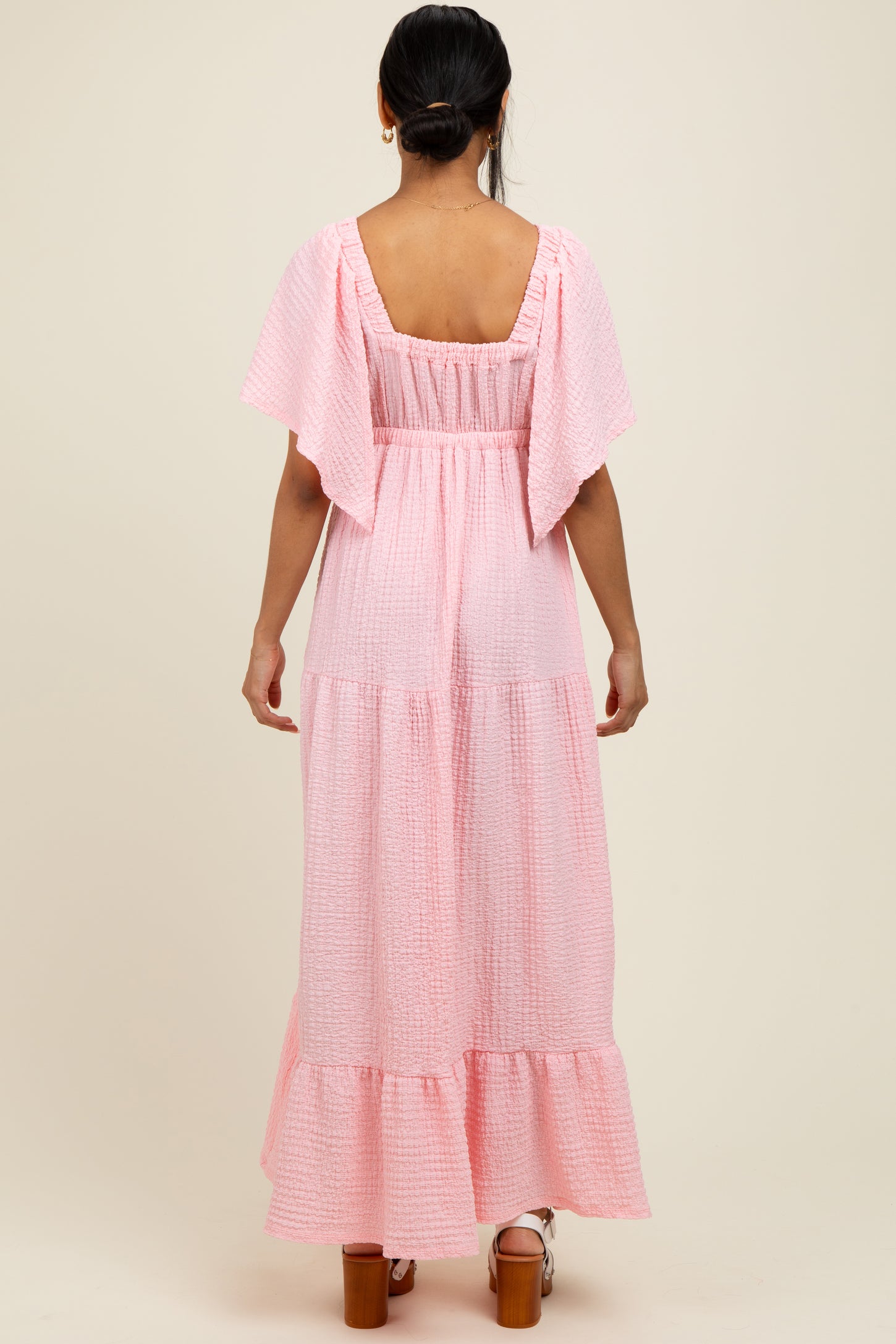 woman wearing a pink tiered maxi dress with flutter sleeves and a smocked back detail
