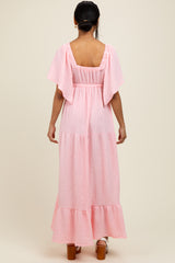 woman wearing a pink tiered maxi dress with flutter sleeves and a smocked back detail