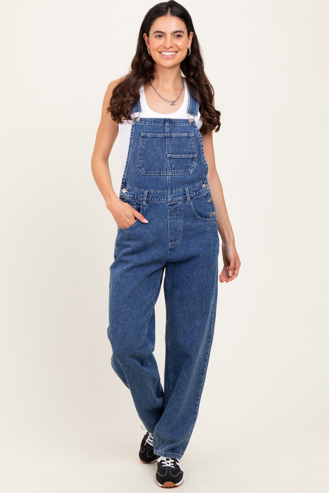 woman wearing a white tank top and blue denim overalls with a relaxed fit and front pockets