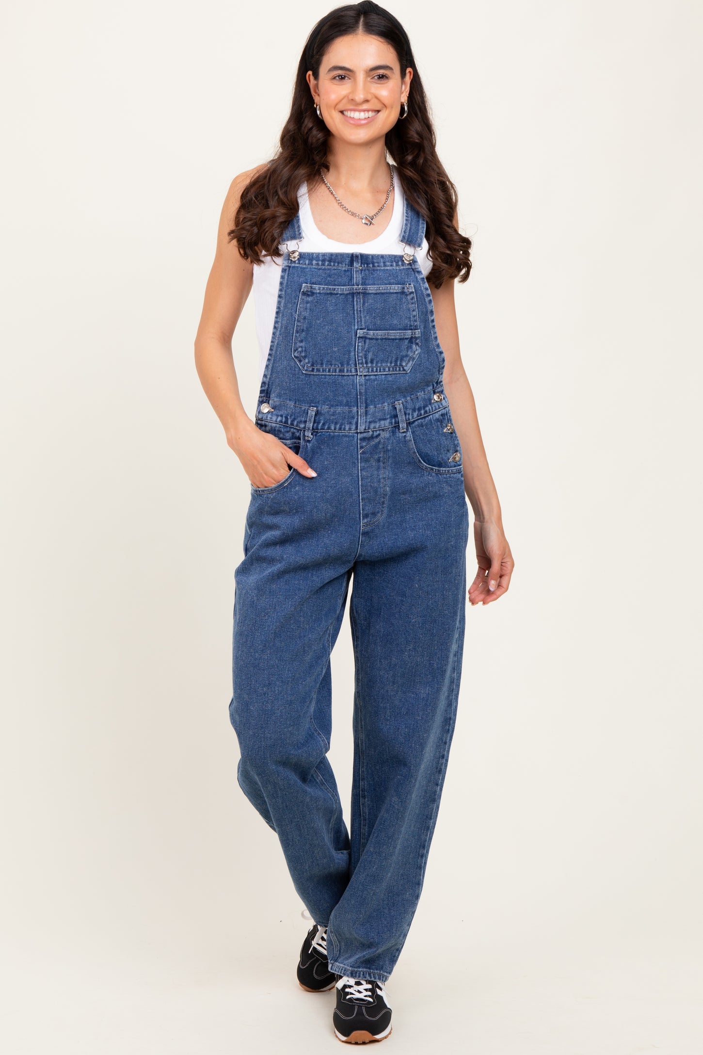 woman wearing a white tank top and blue denim overalls with a relaxed fit and front pockets