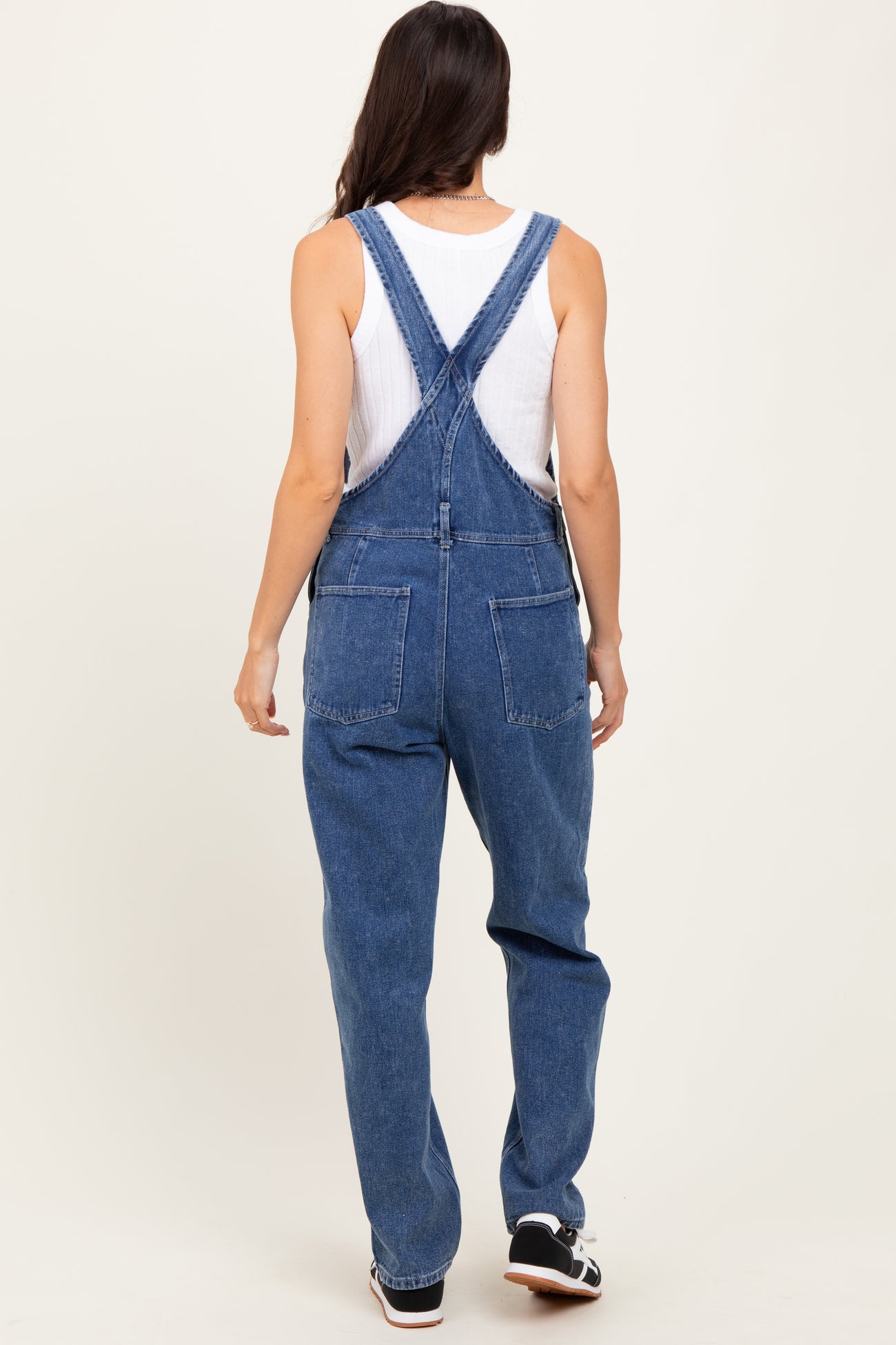woman wearing blue denim overalls over a white tank top, viewed from the back
