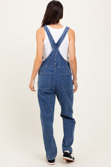 woman wearing blue denim overalls over a white tank top, viewed from the back
