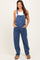 woman wearing a blue denim maternity overall with pockets and a white tank top, posing confidently