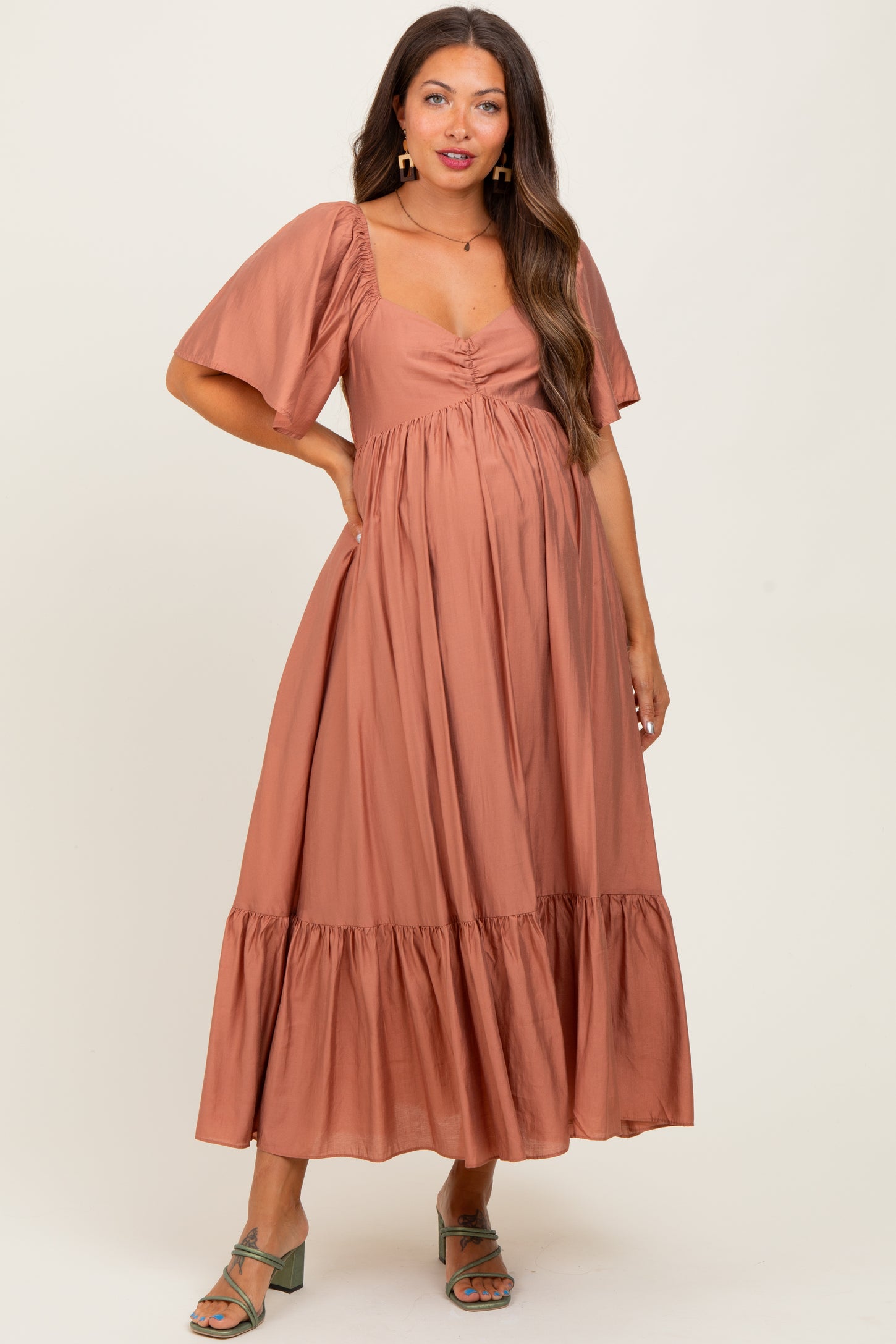 woman wearing a rust-colored maternity maxi dress with short puff sleeves and a tiered hem