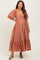 woman wearing a rust-colored maternity maxi dress with short puff sleeves and a tiered hem