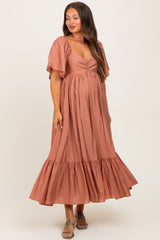 woman wearing a rust-colored maternity dress with flutter sleeves and ruffle hem, showcasing her baby bump